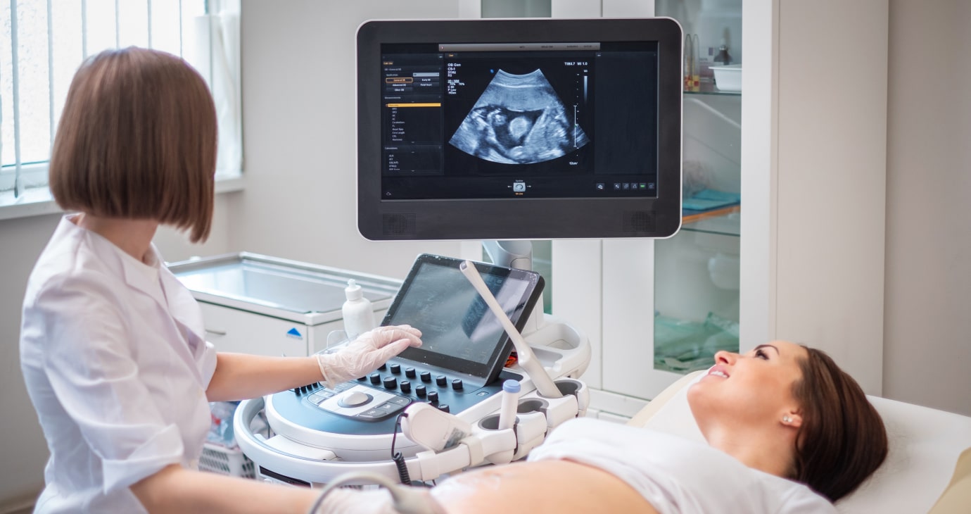 A medical professional, guided by their understanding of women's reproductive health rights, performs an ultrasound on a pregnant woman lying on an examination table, with the image displayed on a monitor.