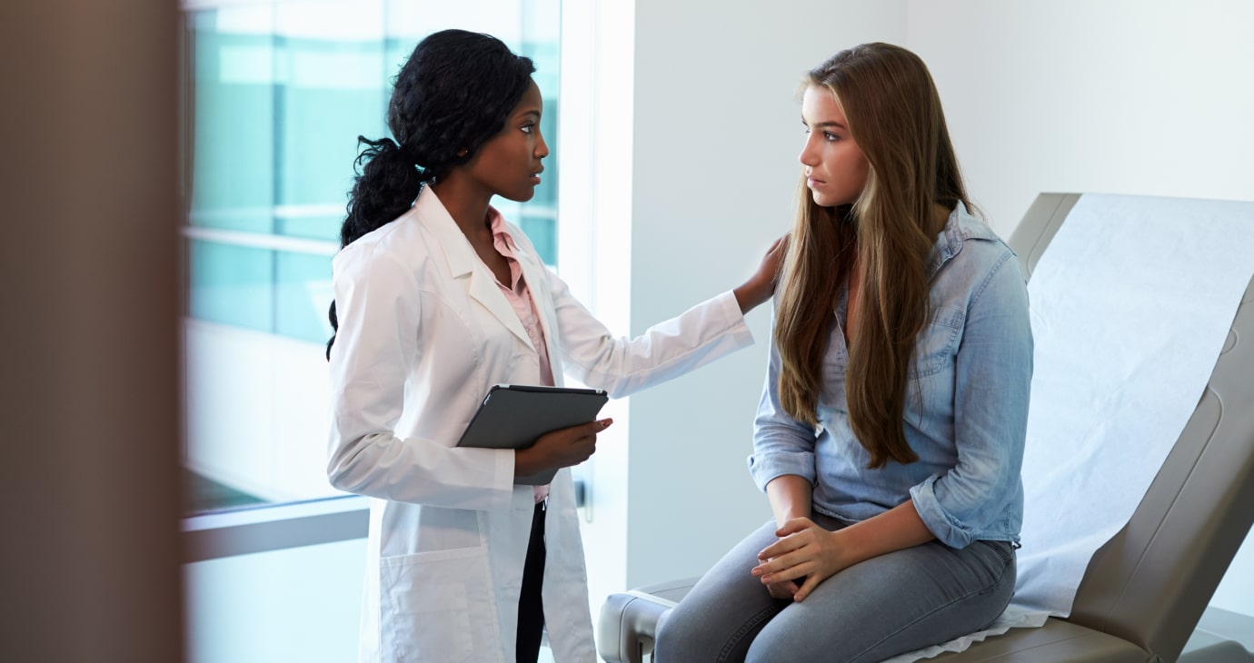 In a serene medical examination room, a doctor in a white coat holds a clipboard, offering comfort to the seated patient. Their focus on patient care creates an empathetic environment that promises improved outcomes for all.