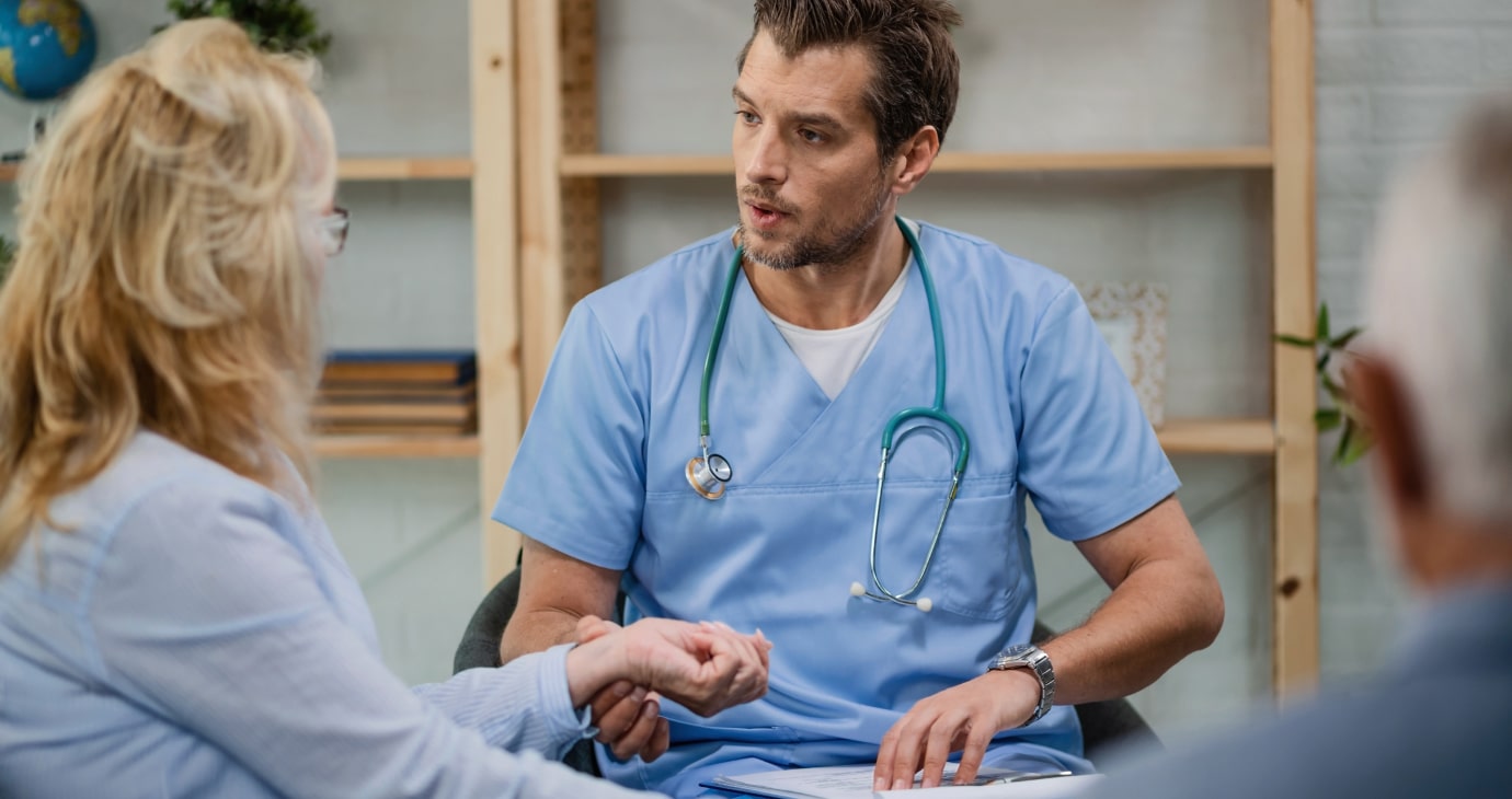 A healthcare professional in blue scrubs holds a patient's wrist during a breast cancer consultation in a medical office, offering insight into neoadjuvant therapies.