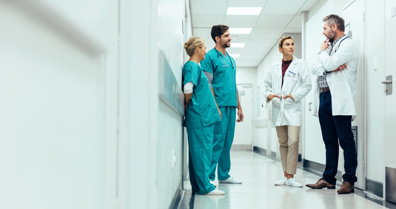 In a bustling hospital hallway, four healthcare professionals—two in scrubs and two in white coats—engage in conversation. With the rise of new treatments like Ozempic, these physicians discuss its impact on patient care and outcomes.